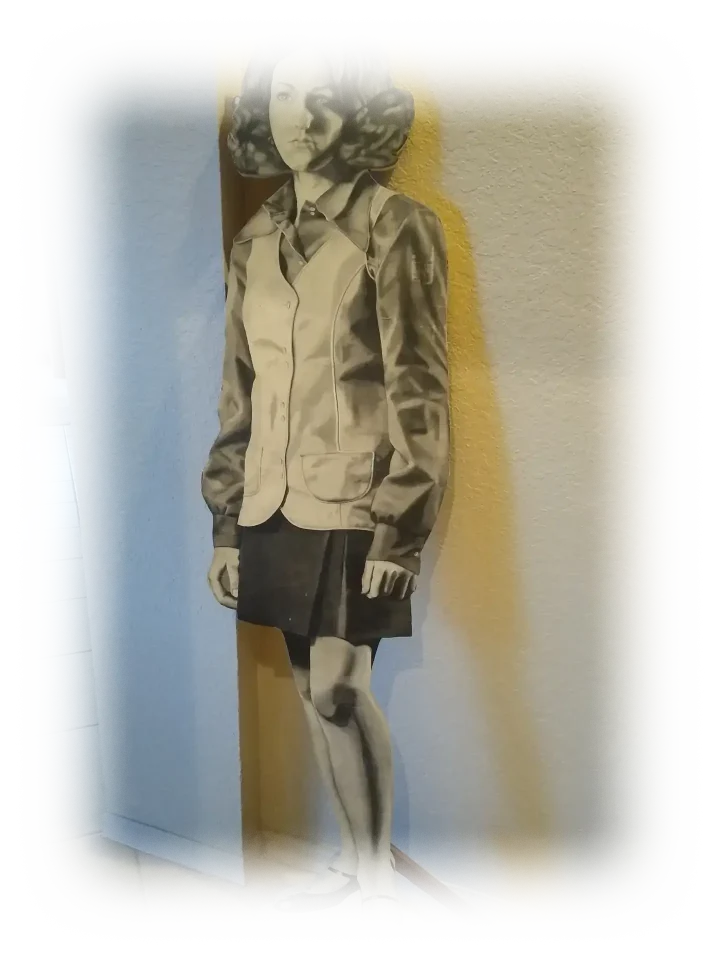 Life-size pencil drawing of the artist when she was 17 on a plywood stand. Completely in gray pencil, the artist is depicted with neck-length hair, big round sunglasses on her head, a long collared shirt and buttoned vest, a skirt and airy, heeled shoes.