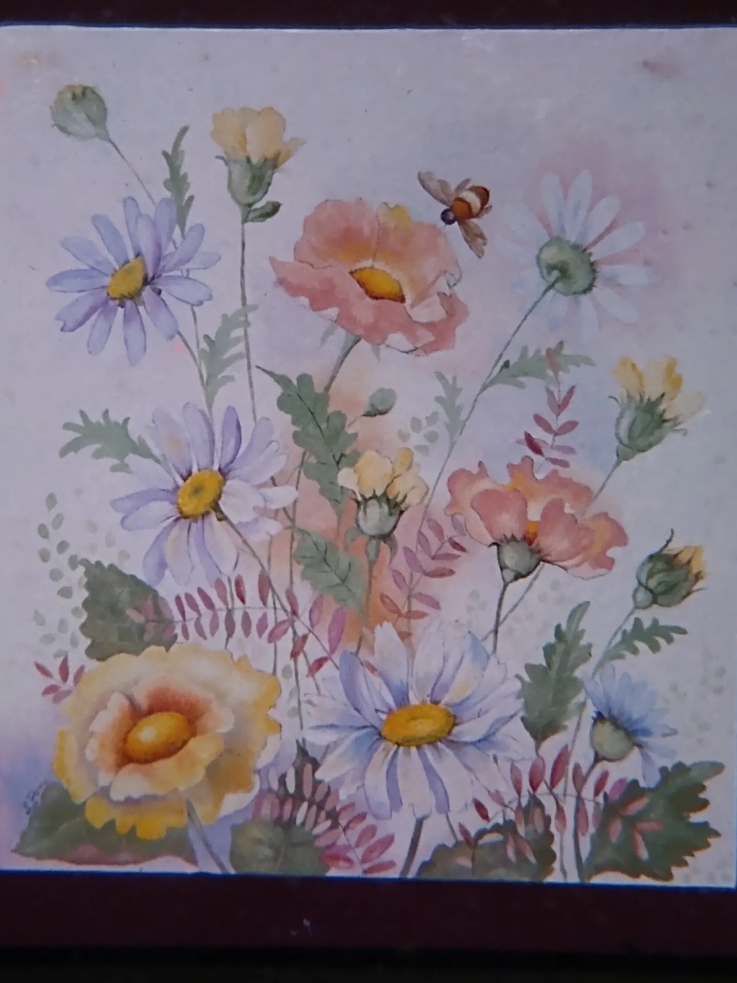 A large bee flies among pastel-colored flowers set against a whitish background into which the leaves seem to fade, as if it were fog.